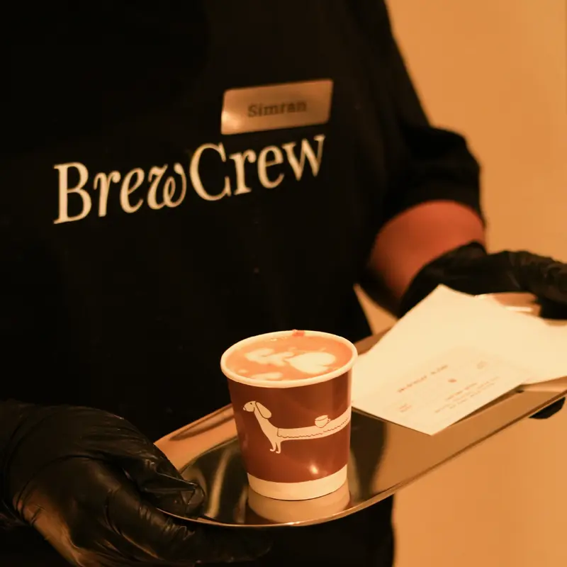 A barista from the Unlock Everyday Brew Crew serving a latte